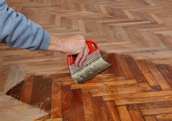varnishing of oak parquet floor, workers hand and brush